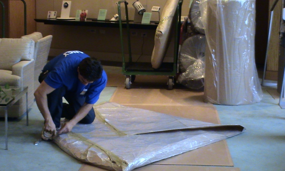 a professional mover kneeling on a floor to carefully wrap and tape a large object