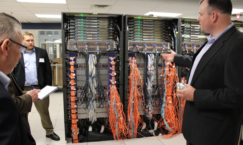 businessman gestures toward open server racks filled with dense network cabling