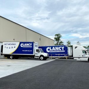 Several Clancy moving trucks parked outside a large warehouse