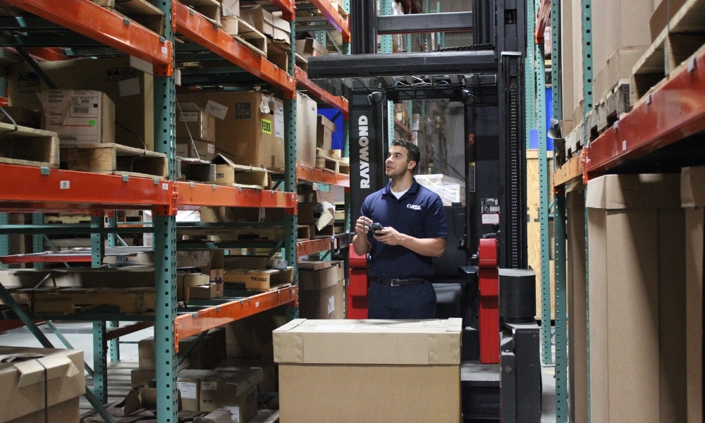 a warehouse worker stands next to a Raymond forklift