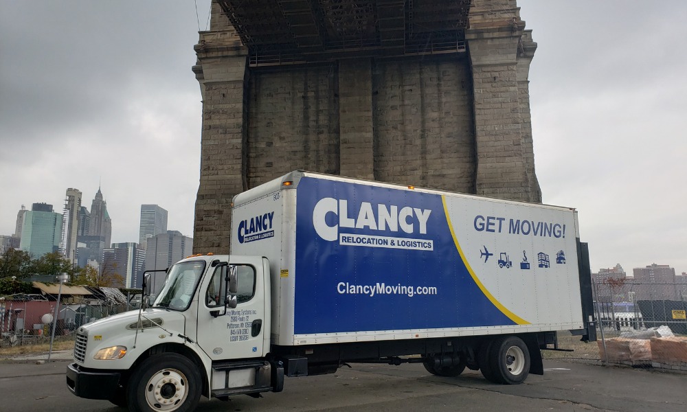 A Clancy Relocation & Logistics moving truck parked beneath a large stone bridge