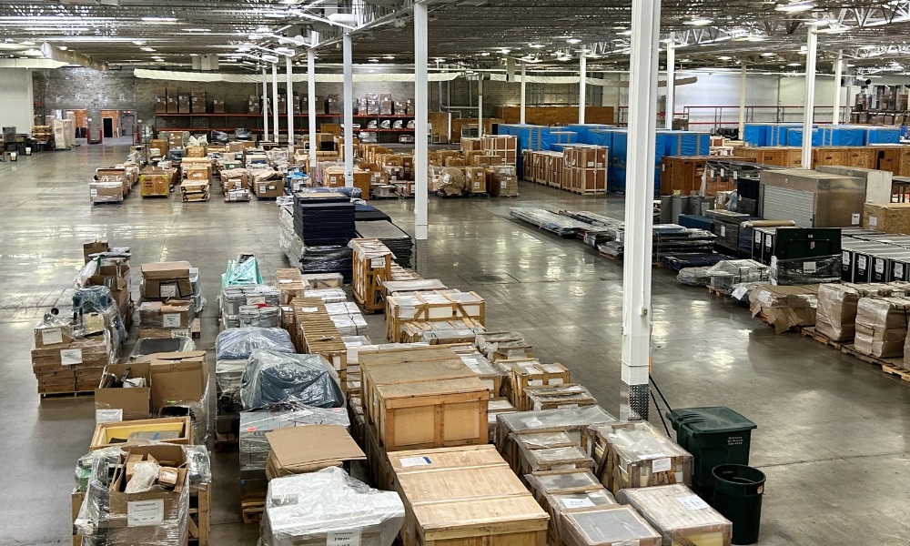 An expansive warehouse filled with stored crates, wrapped pallets, and equipment