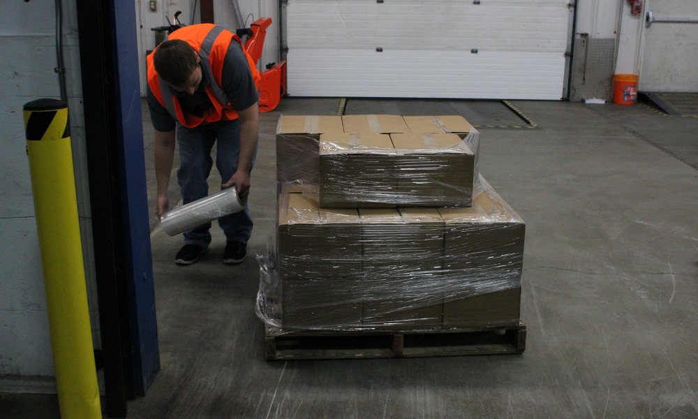Worker in an orange safety vest wrapping a pallet of cardboard boxes