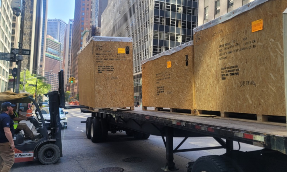 Forklift loading large wooden shipping crates onto a flatbed trailer